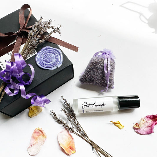 Just Lavender natural perfume gift set featuring lavender essential oil rollerball, dried lavender sachet, and mini lavender dried flower, with an elegant black gift box and dried lavender flowers and rose petals in the background.