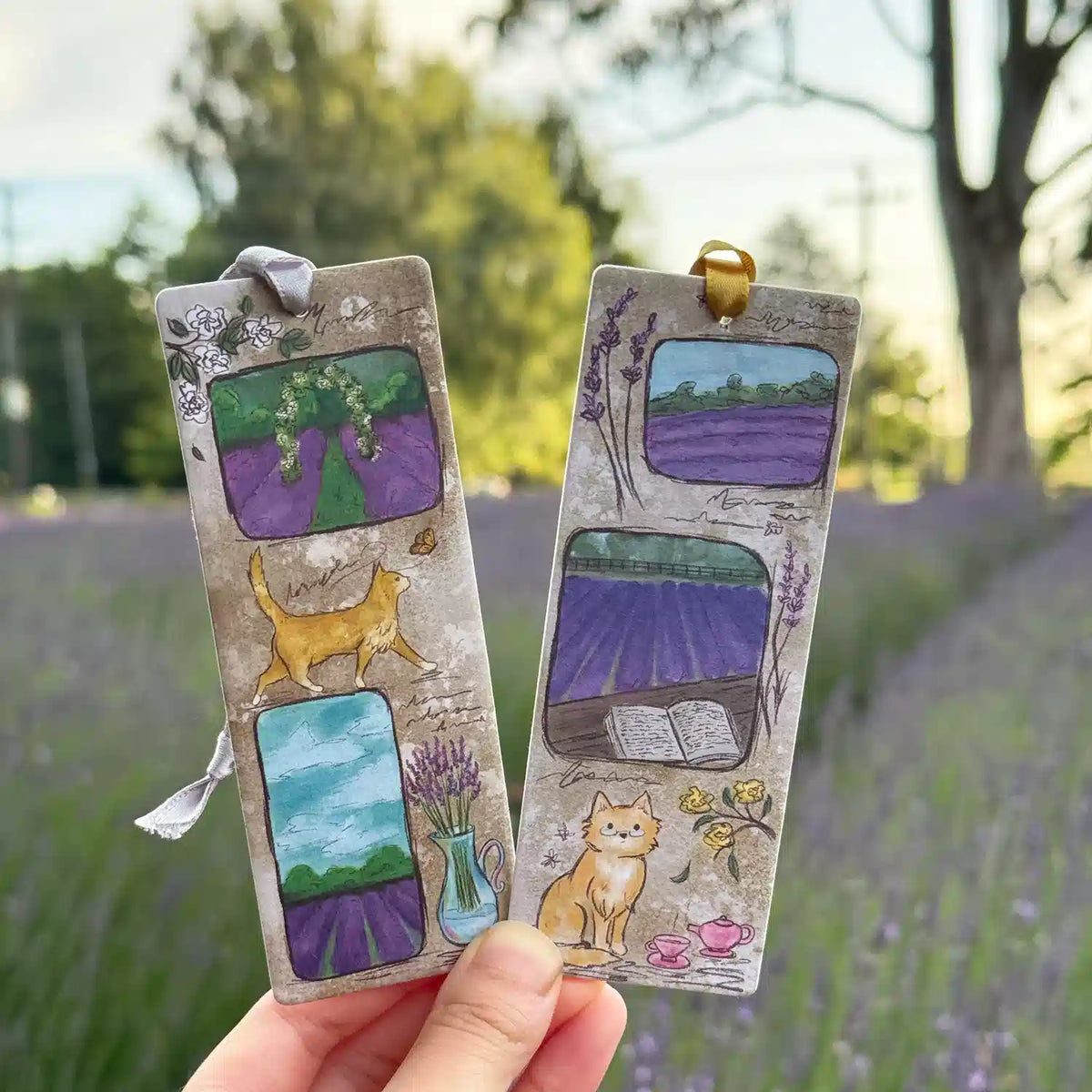 Two Orange Cat Lavender Field Scented Bookmarks with lavender field scenes and a ginger cat, held in a lavender field