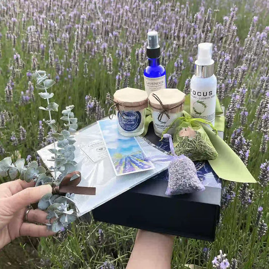 Calming Sleep Gift Set displayed against a vibrant purple lavender field, featuring items infused with essential oils: Lavender Pillow Mist, Focus Aromatherapy Spray, Lavender Sachets, Soy Candles, Dried Eucalyptus Bundle, and a Lavender Field Bookmark.