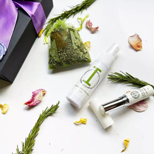Close-up view of "Natural Lavender Insect Repellent - Travel Size, Natural Lip Balm for Chapped Lips, Eucalyptus, Rosemary & Lavender Sachet," with a background of purple ribbon black gift box, rosemary leaves, and rose petals.