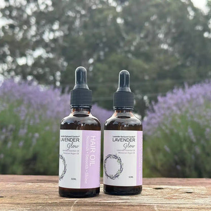Two bottles of lavender hair oil placed on a wooden bench against blooming lavender plants.
