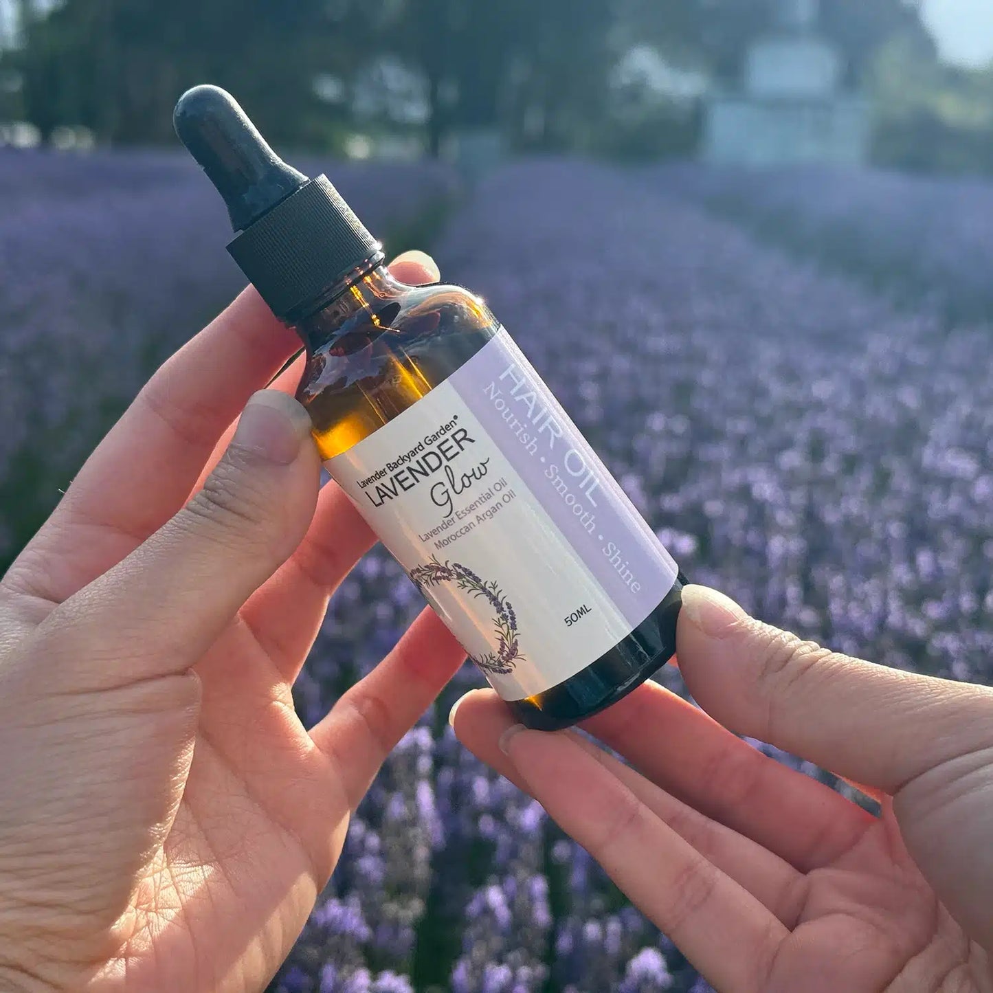 Hand holding a lavender hair oil bottle against a sunset lavender field.